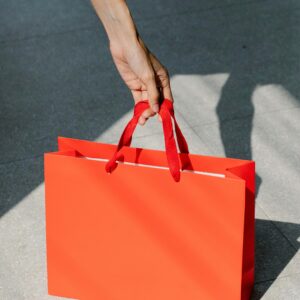 High angle of crop anonymous female buyer taking red paper bag with purchase in sunshine